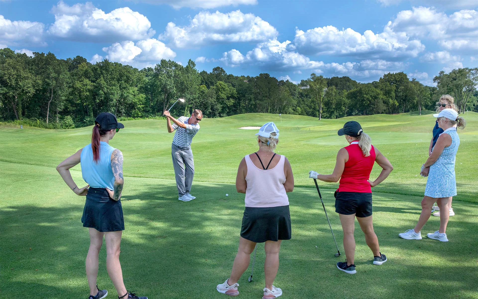 A PGA-Certified teaching pro providing a clinic to adult members of an Invited Club on the driving range.