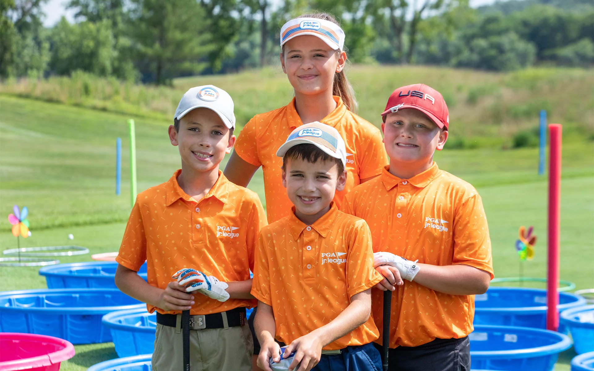 Immerse your child in engaging golf experiences with a membership at an Invited Club – Image of four young golfers in front of specially designed game buckets for skill improvement and entertainment.