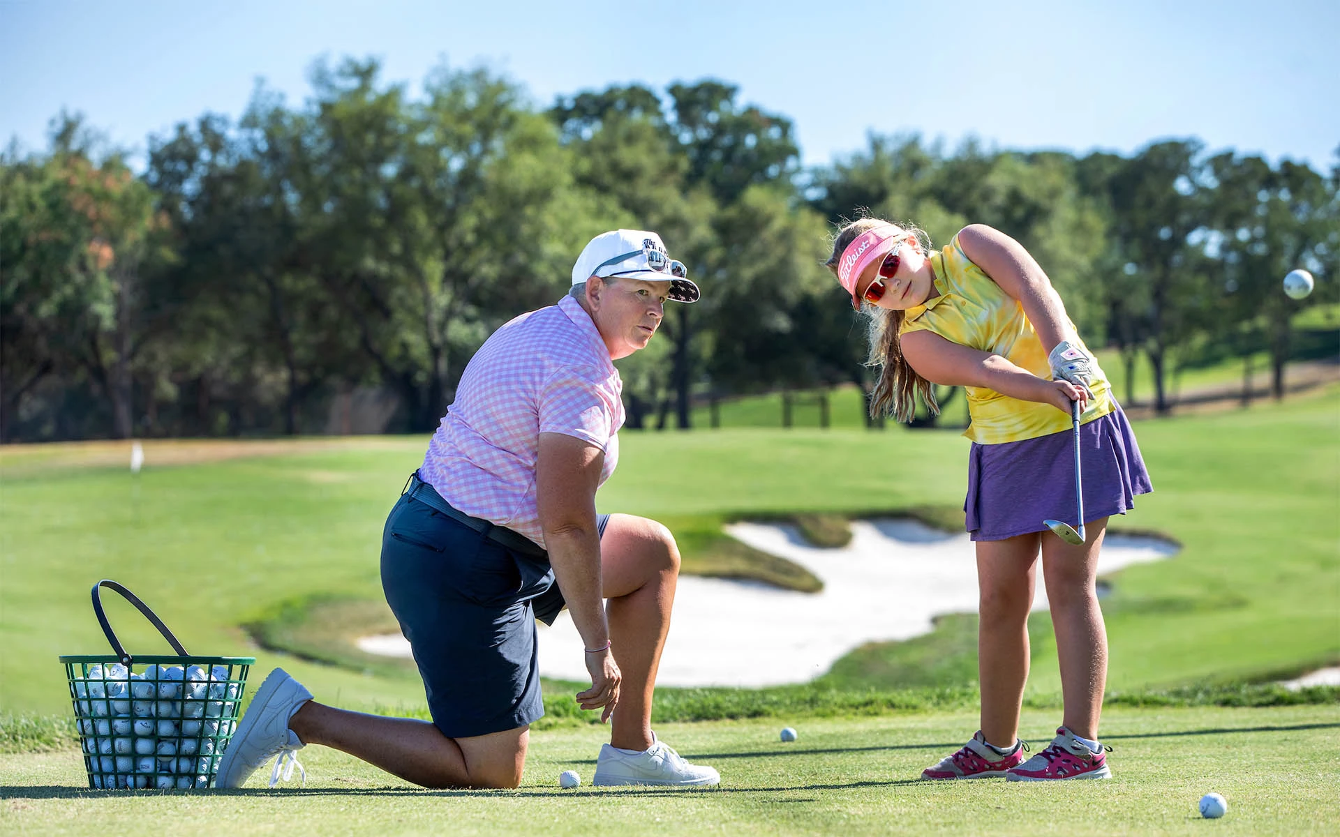 One of Invited's dedicated golf coaches providing personalized instruction to a young girl during a youth golf lesson, teaching her the basics of the game.