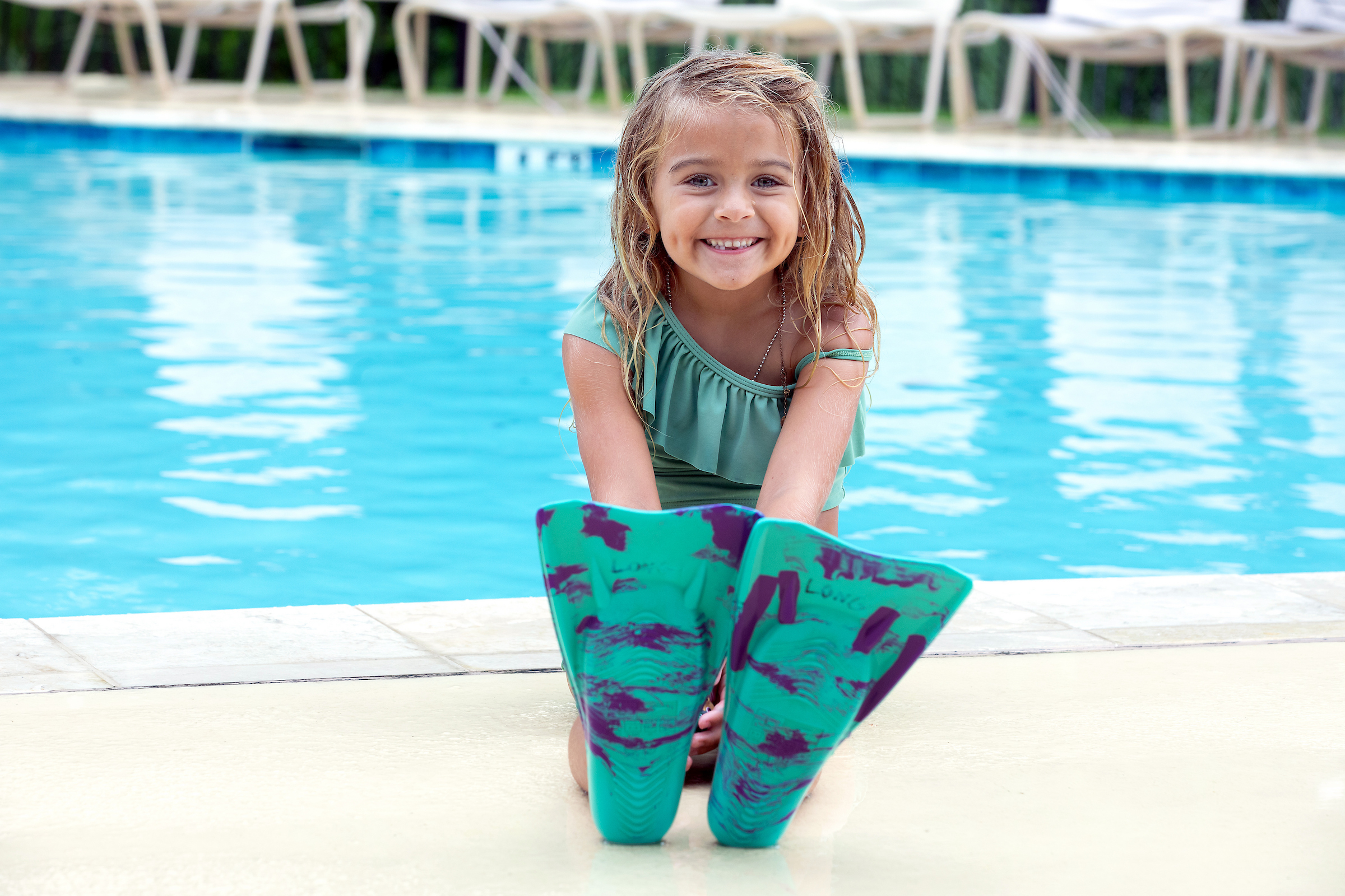 Little girl sitting by pool with flippers on