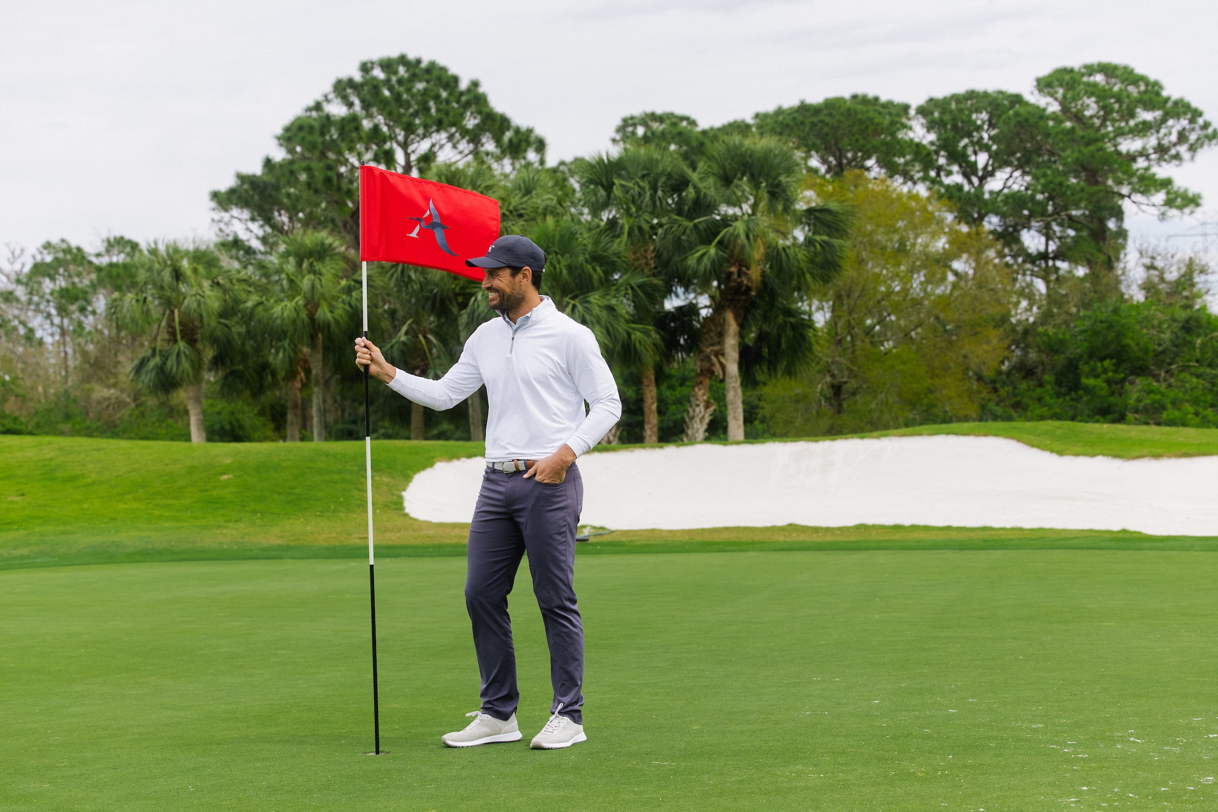 Man standing on a golf course holding a hole flag