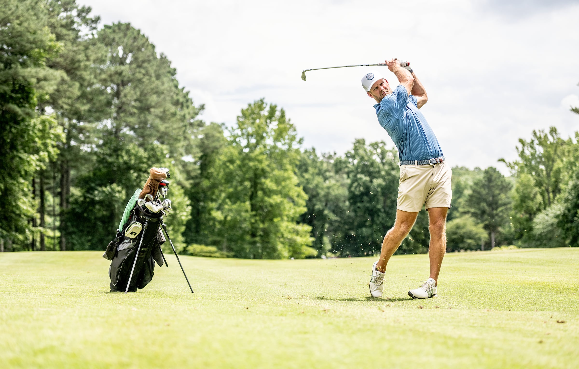 Golfer swinging club with golf bag nearby
