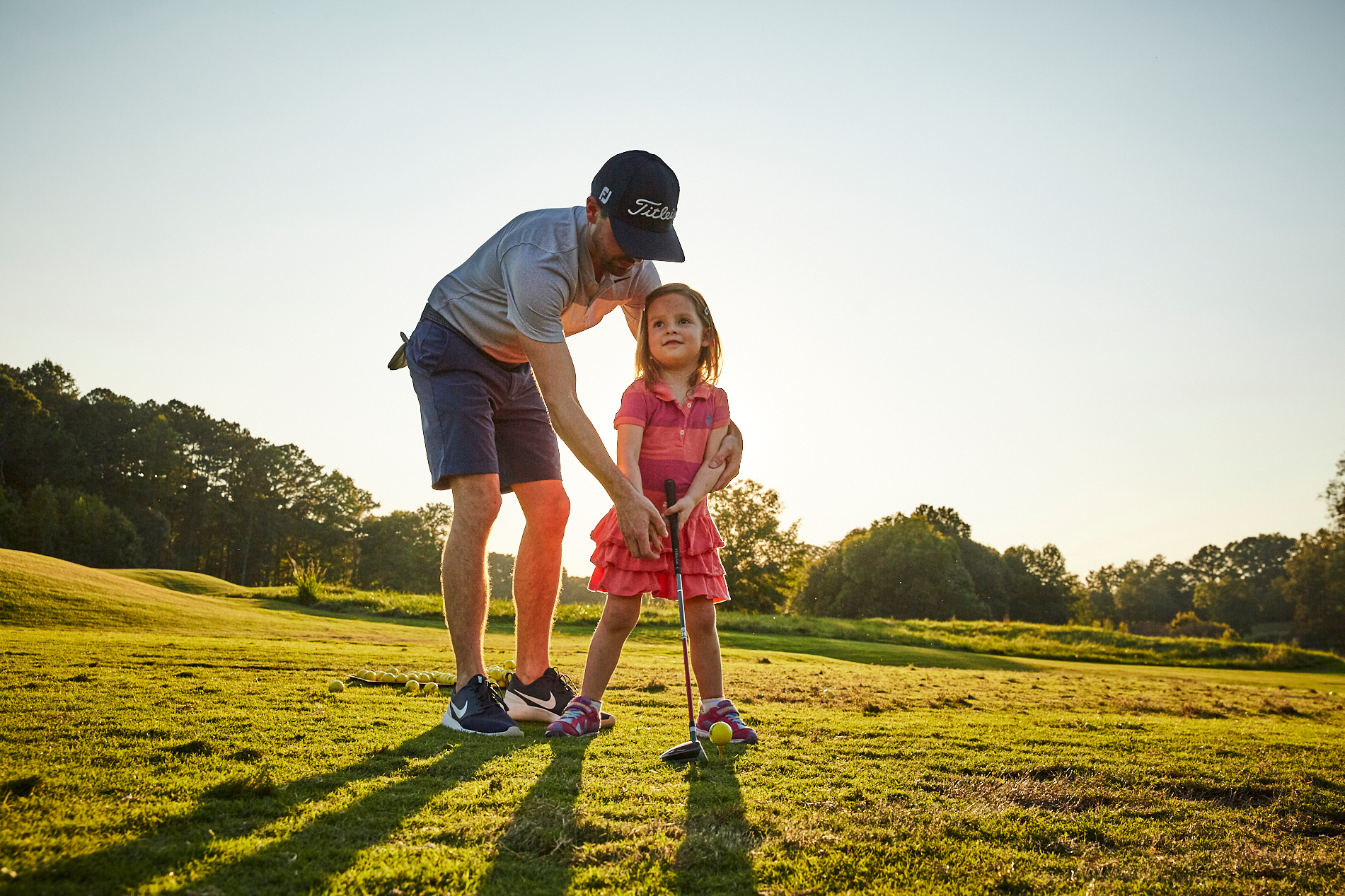 Father instructing young daughter how to swing her golf club