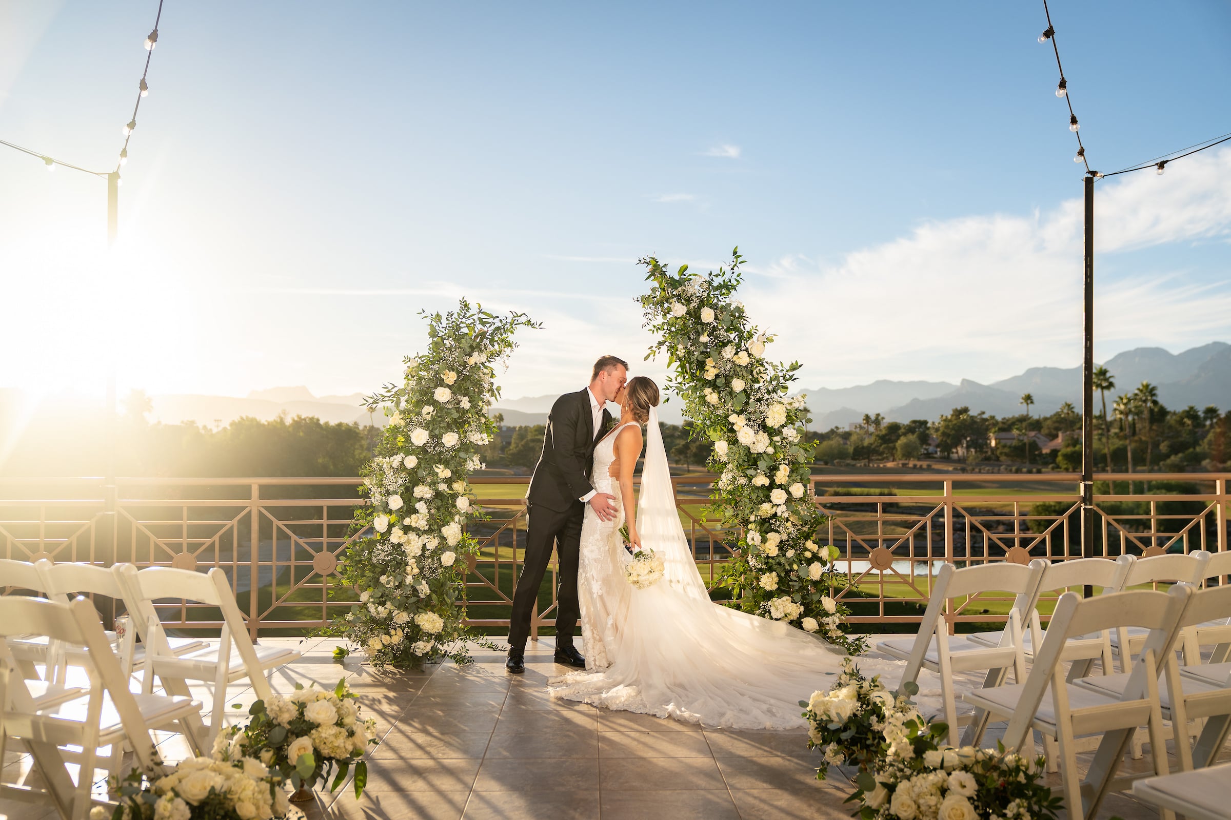 Bride & Groom standing under flower arch at outdoor ceremony