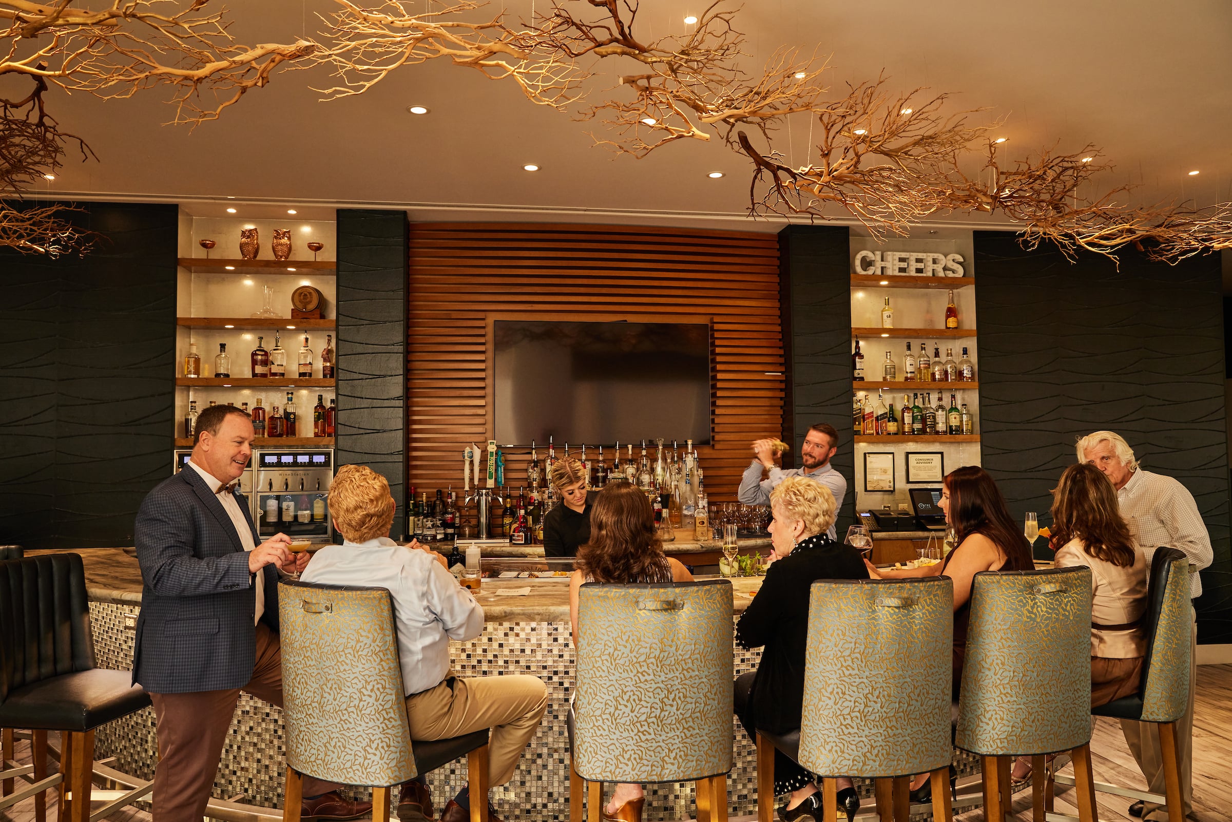 Men & Women seated at the bar with a Bartender making drinks