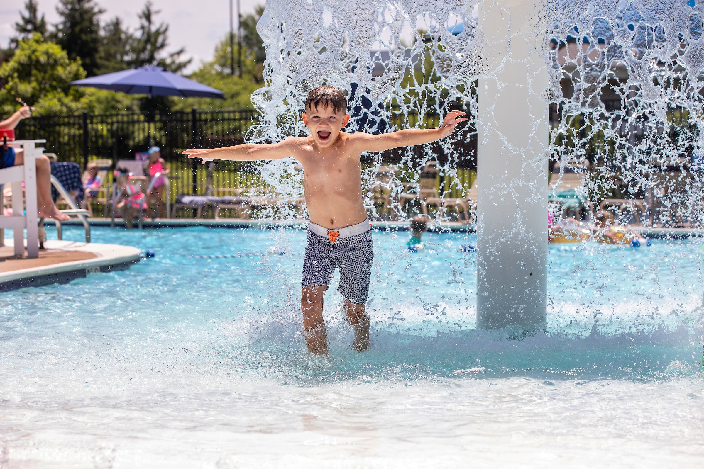 young boy running through water fountain at pool