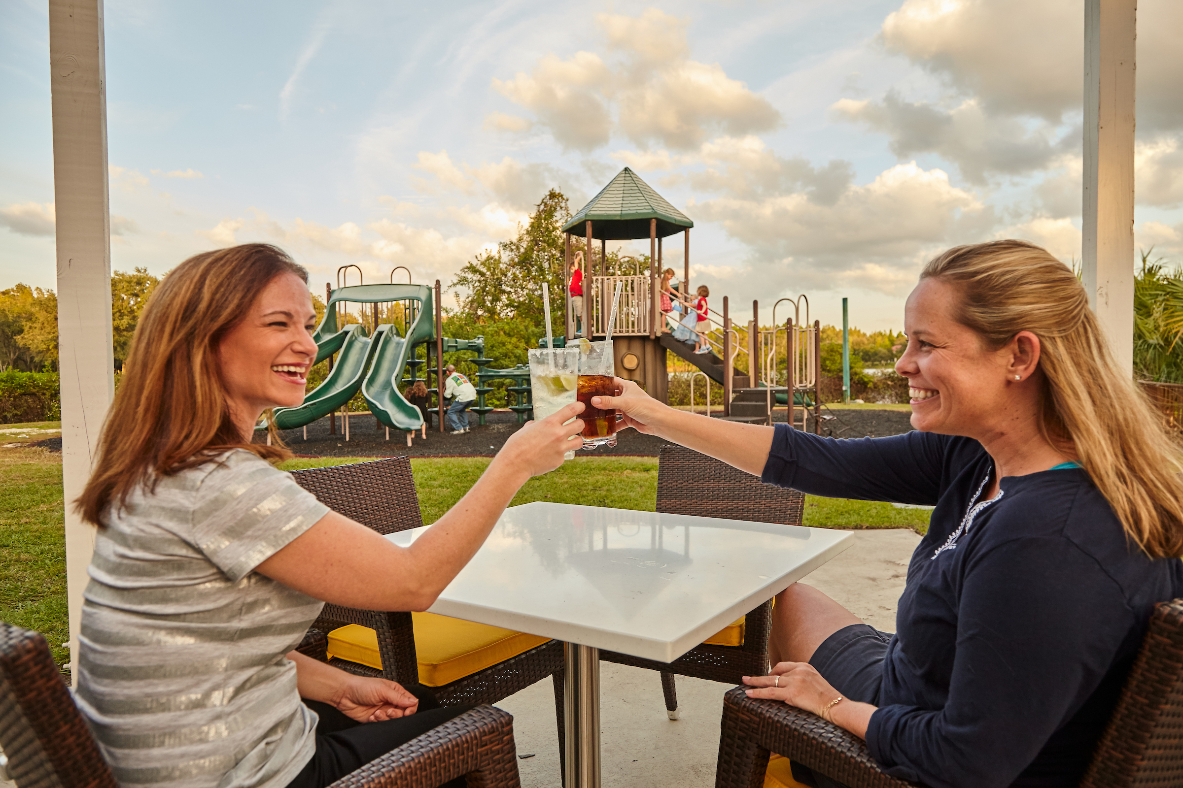 Two mothers cheering drinks while kids play in background