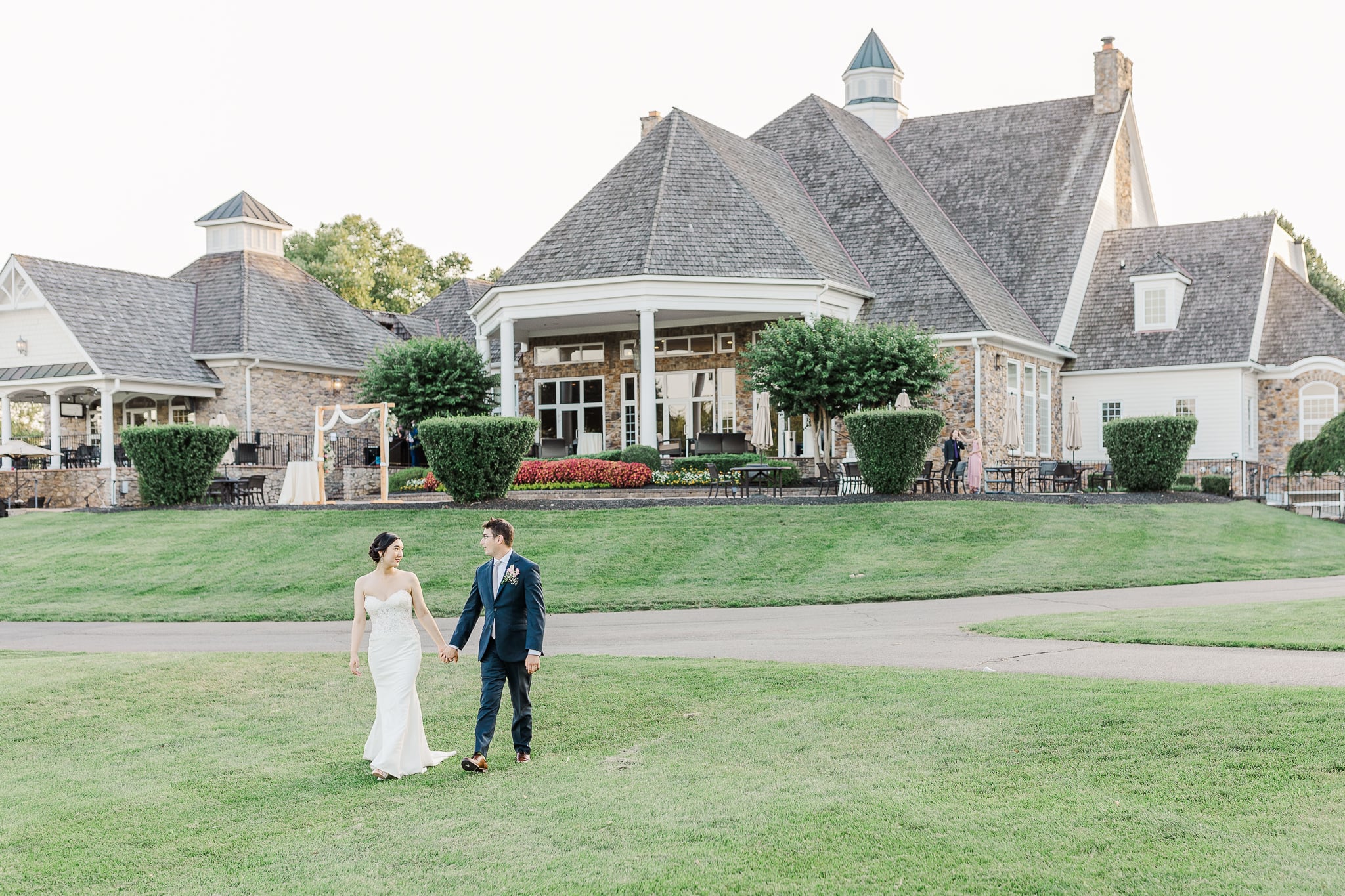 bride and groom walking on golf course by a clubhouse