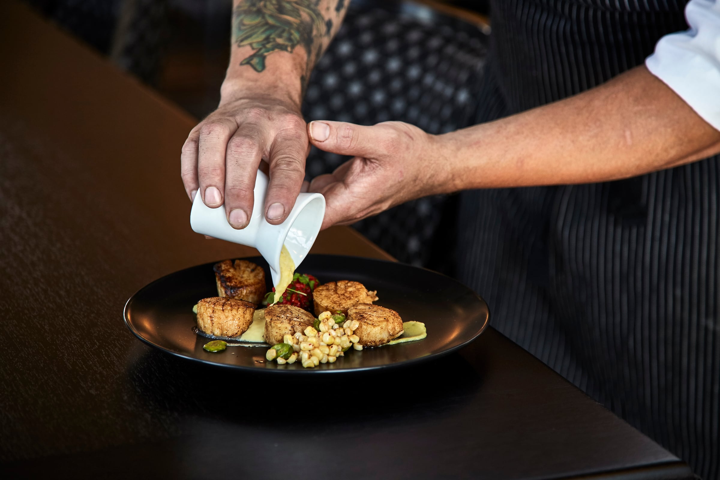 Sauce being poured on a plate of scallops