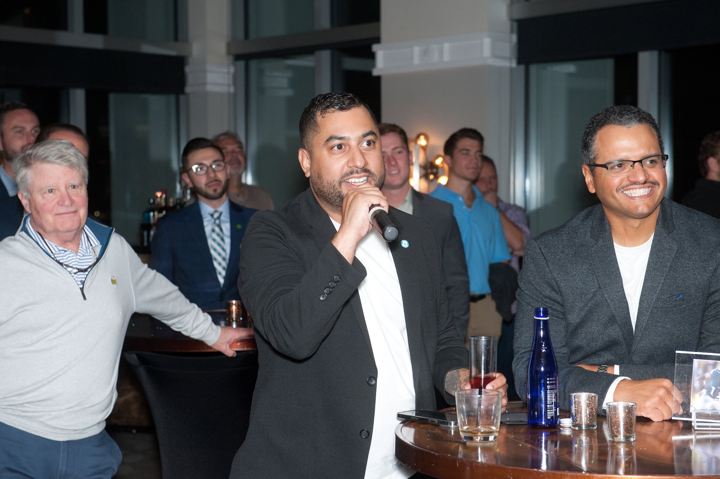 Three men at Speaking event, center man has a microphone