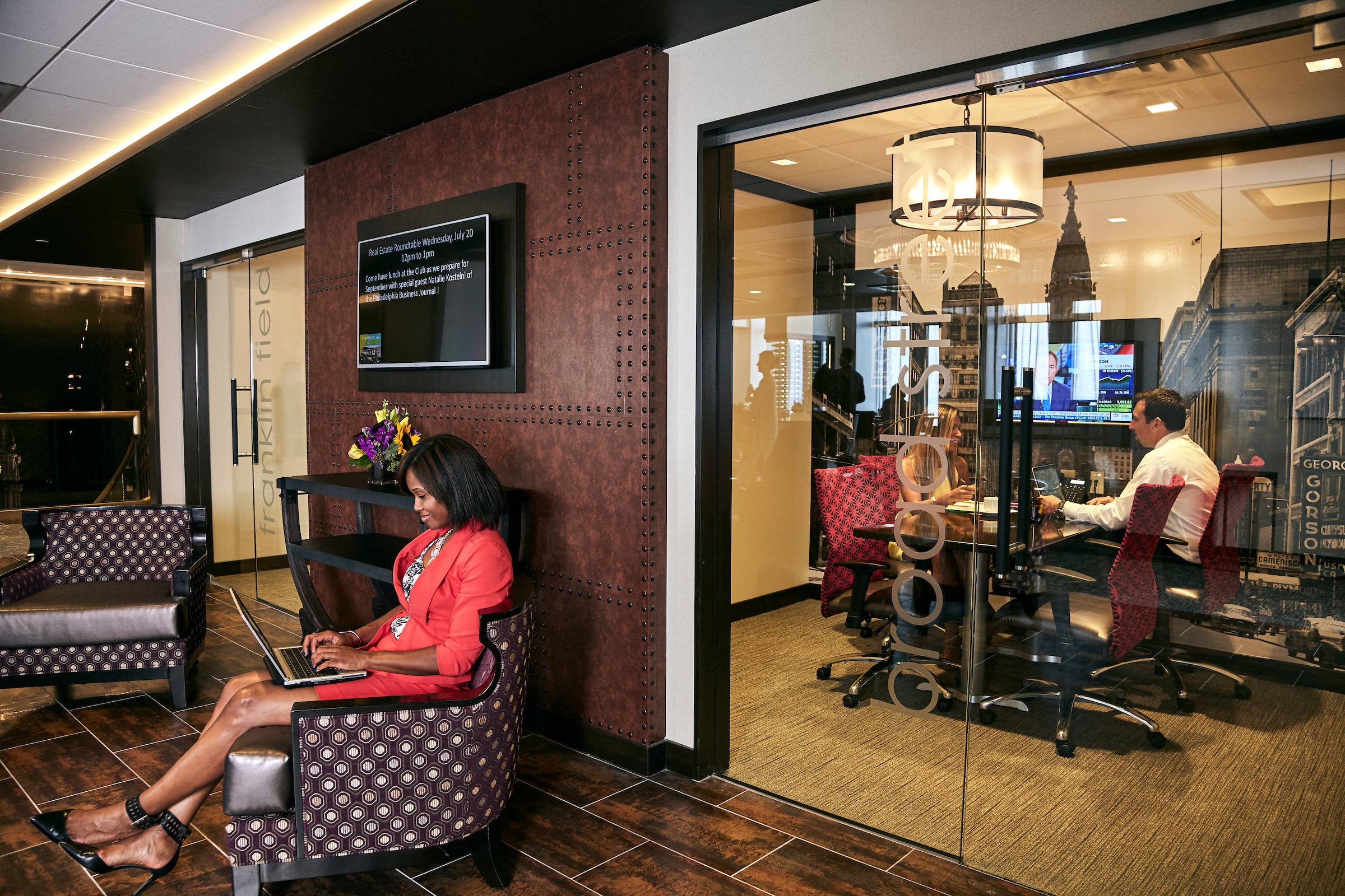 Woman sitting in Pyramid Club lobby also a man & woman in a private office room