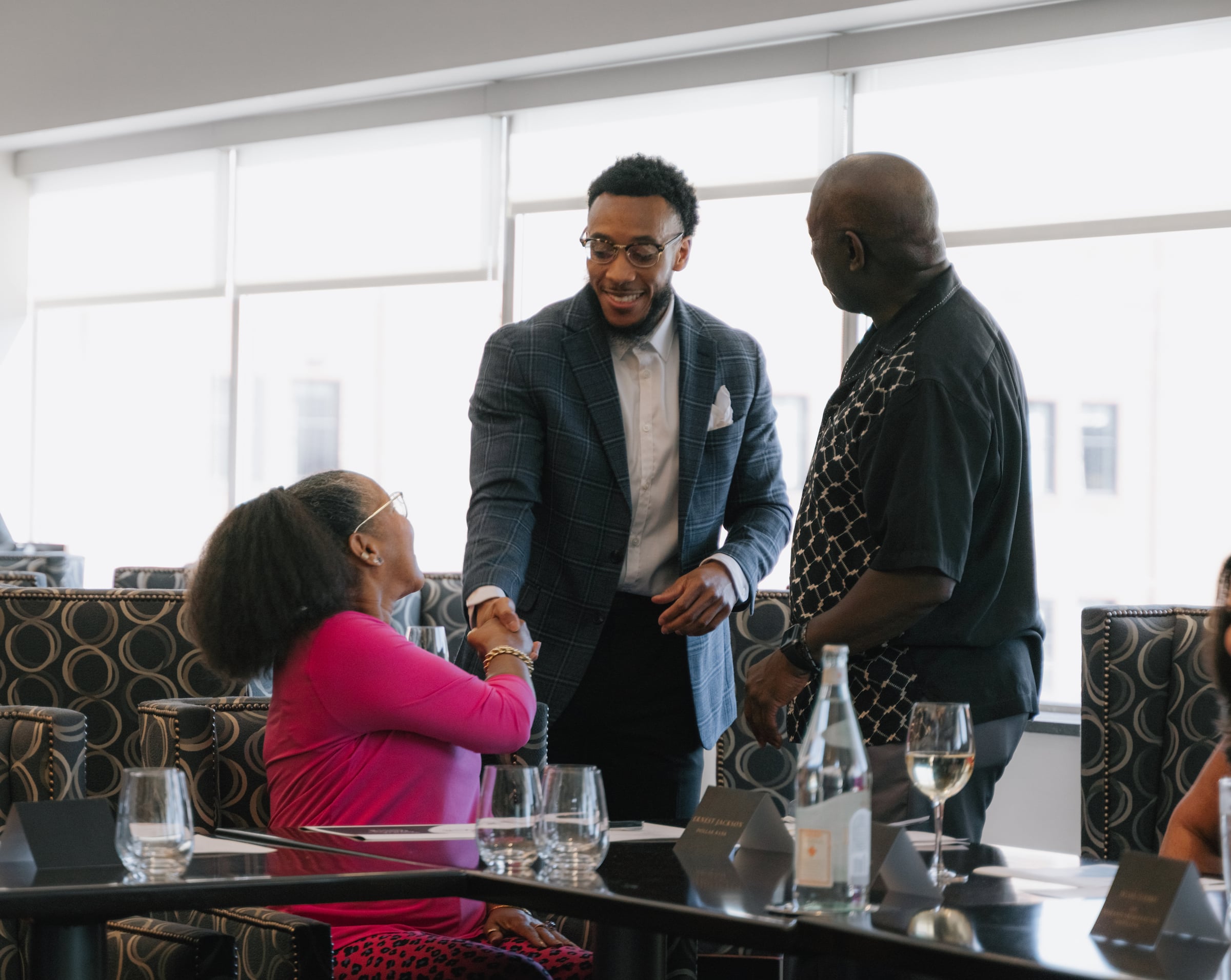 Two men standing greeting a woman who is sitting