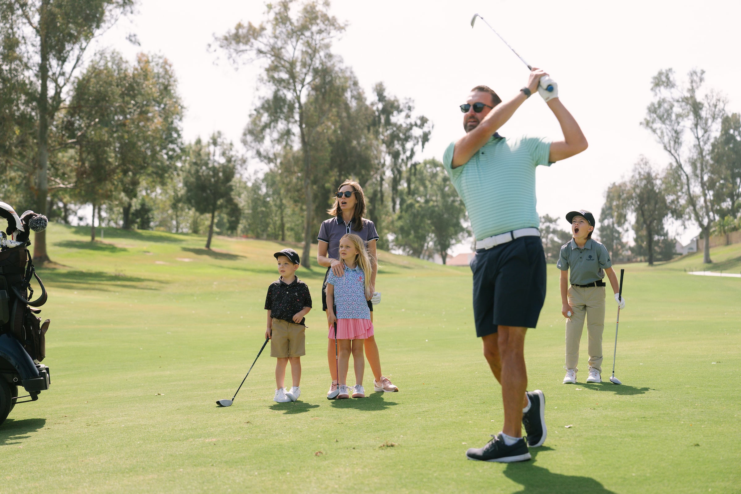 Dad hitting a golf ball with wife and kids in the background watching