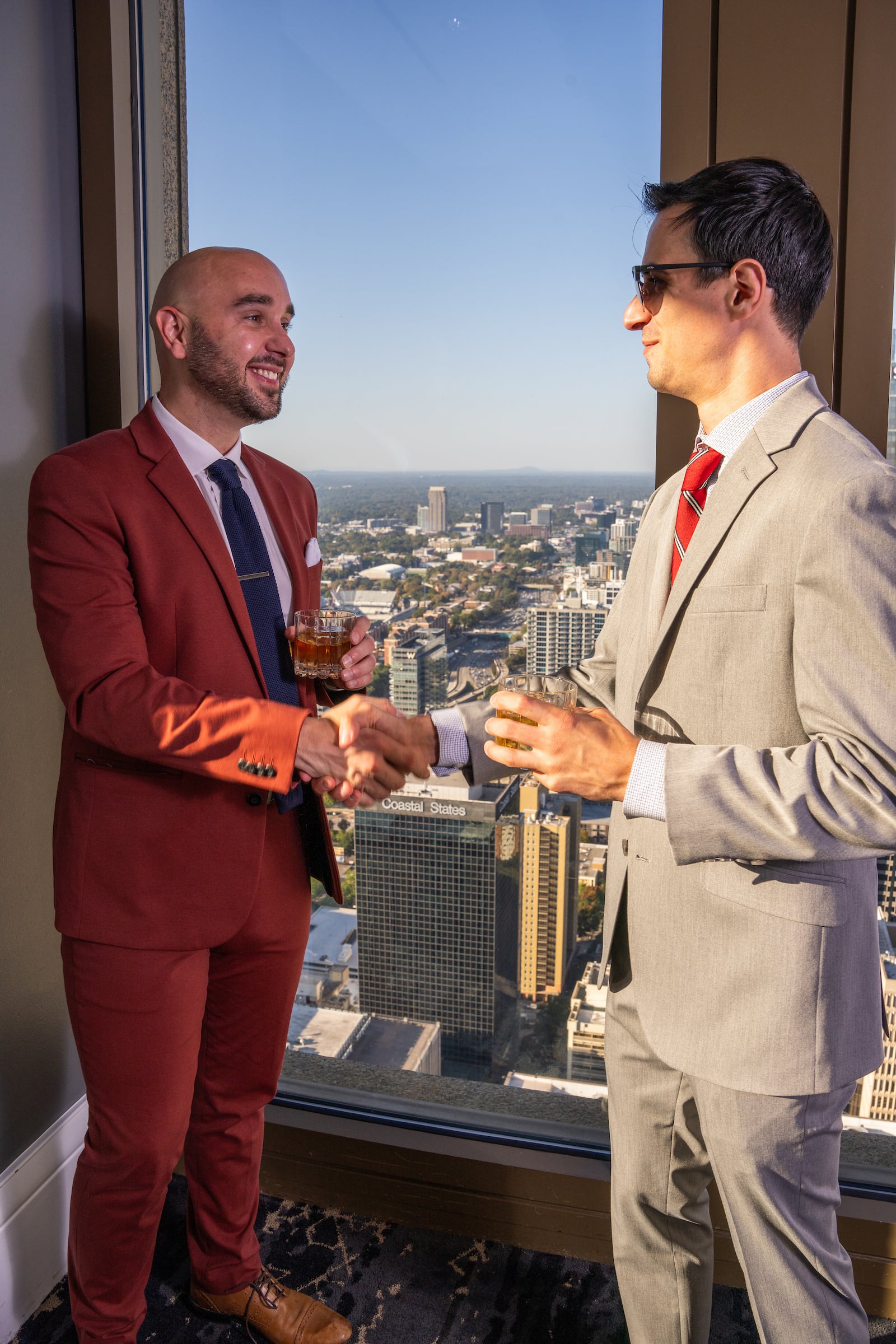 Two men drinking while standing next to a window