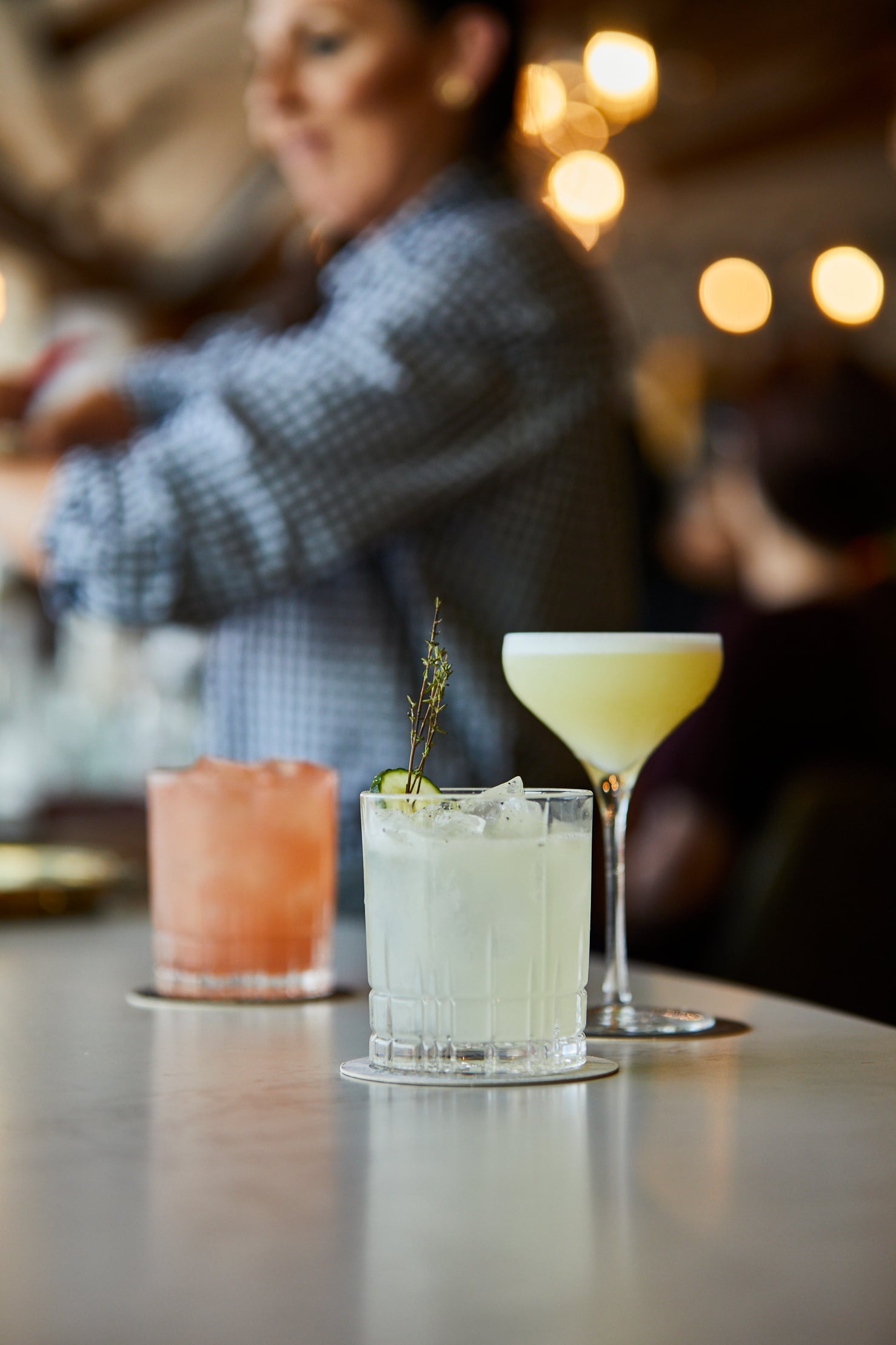 Three cocktails on bar counter with woman in background