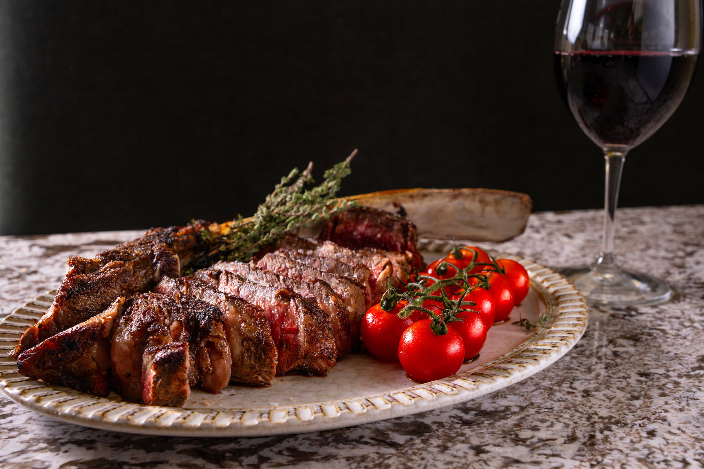 Plate of sliced steak with cherry tomatoes & a glass of red wine
