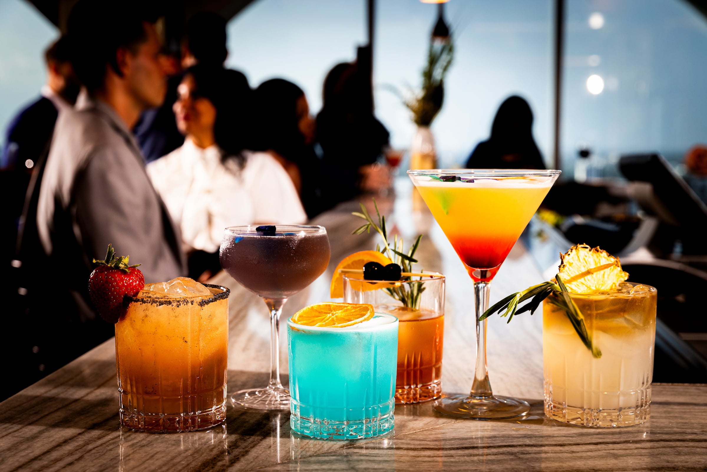 Six cocktails lined up on a bar
