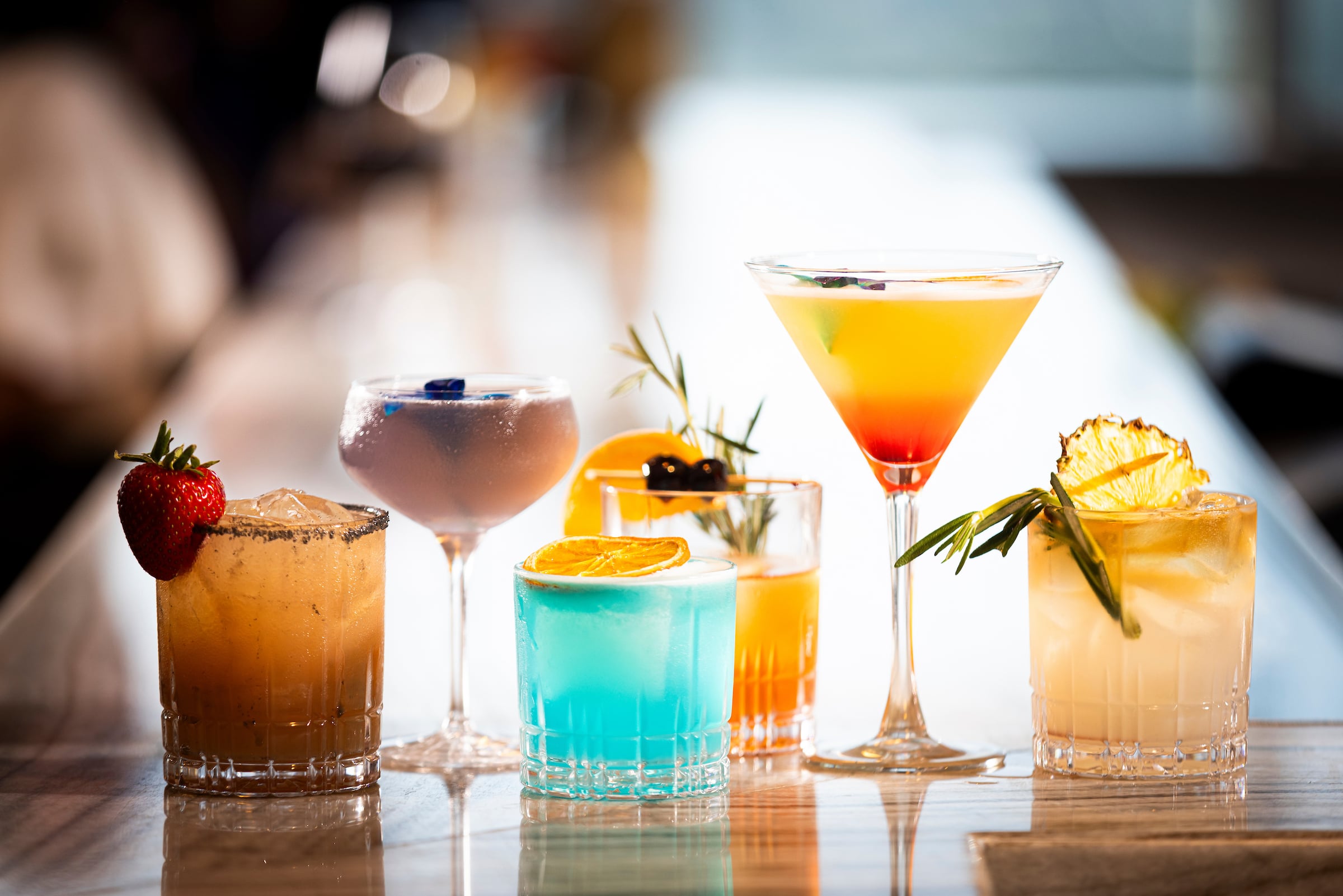 Six cocktails lined up on a bar