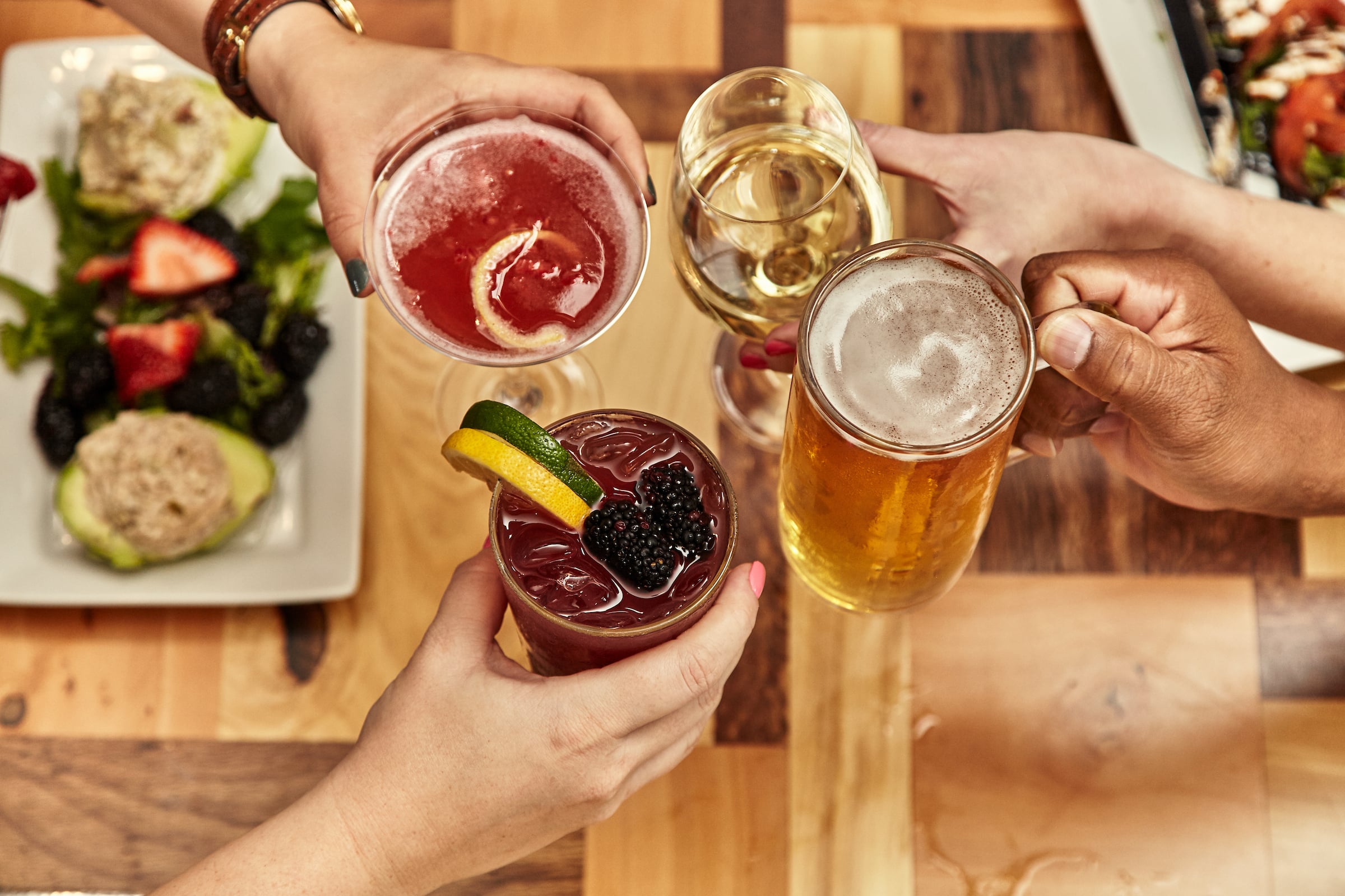 Four hands holding drinks with food on a table