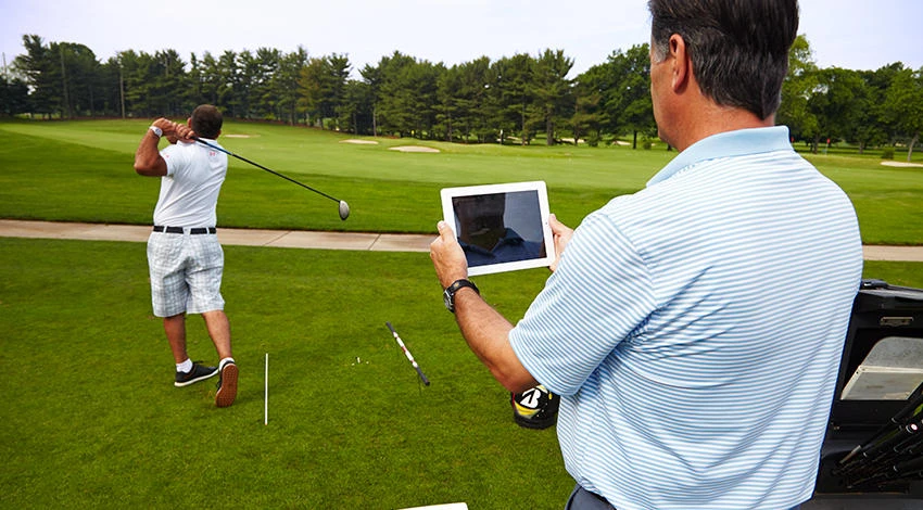 Golfers playing while one holds a tablet