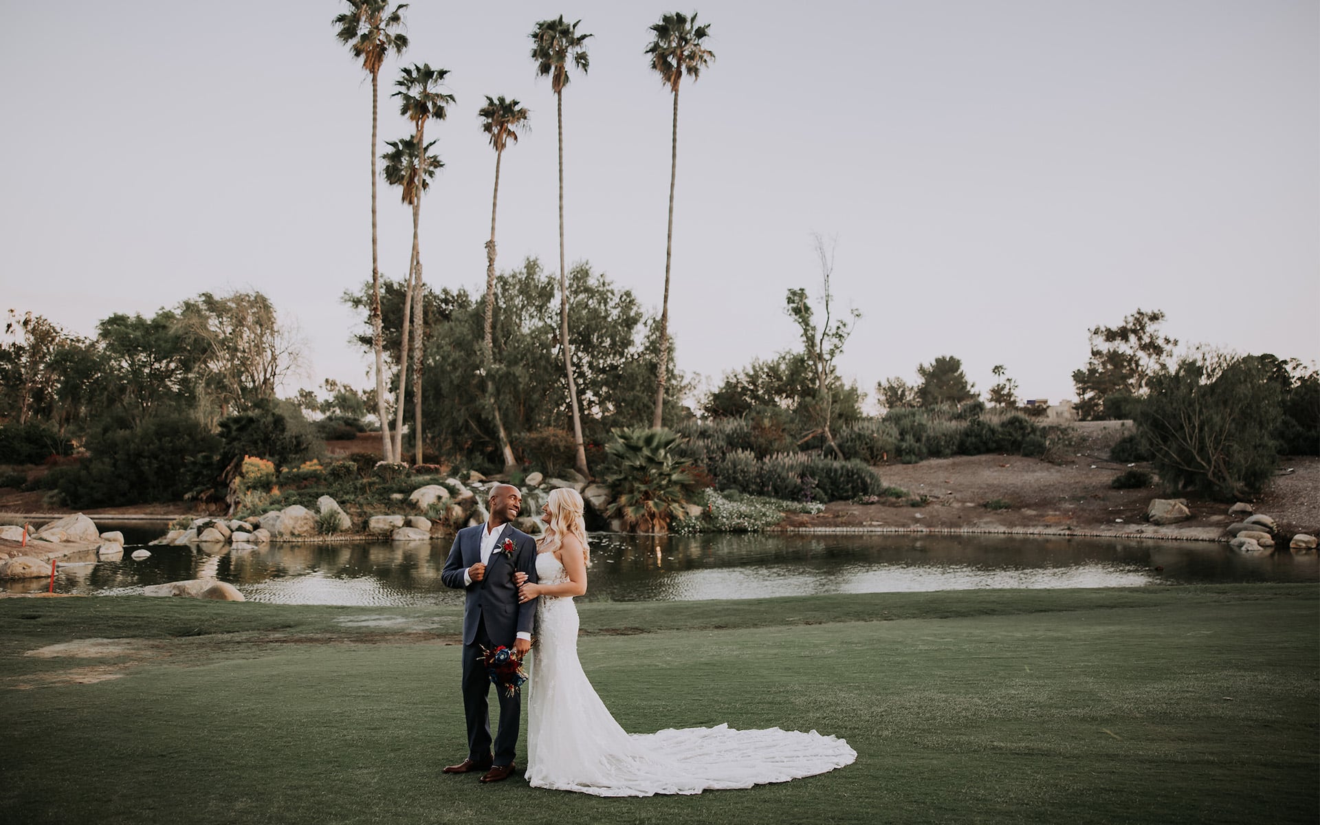 An interracial couple standing on a golf course taking photos on their wedding day 